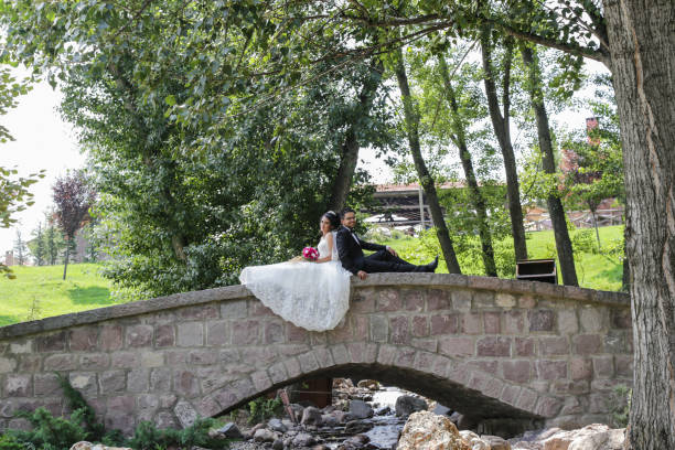 Bride and groom sitting old romantic bridge over river.