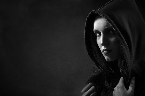 serious woman in hood looking at camera on black background with copyspace monochrome