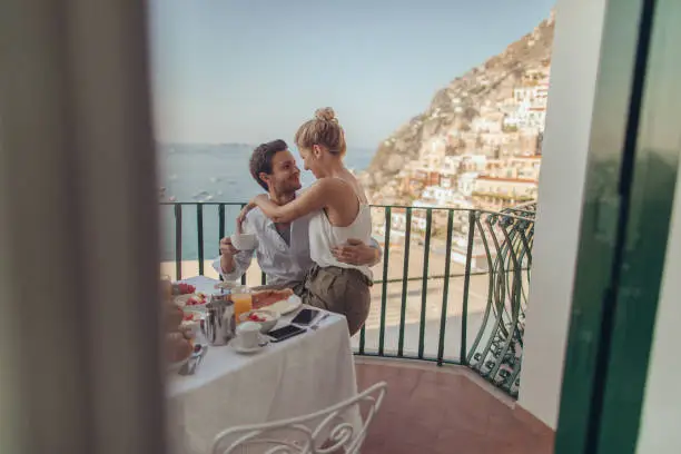 Photo of a beautiful loving couple having breakfast on the terrace with a view of amazing Positano, Italy