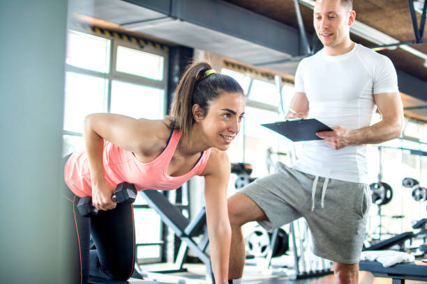 fille de remise en forme ayant des exercices de musculation avec l’aide de l’entraîneur dans une salle de sport. - gym muscular build weights two people photos et images de collection