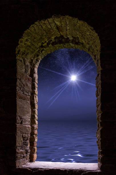 istock Bright star with rays on the dark night sky covered by other stars with wavy water surface which reflects all the pattern visible through an old ancient window. 868231228