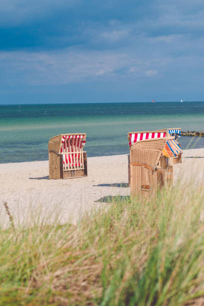 Red striped roofed chairs on empty sandy beach in Travemunde. Grass bush in foreground. Germany