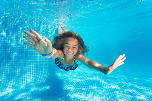 Portrait of preteen girl diving with fun in blue pool