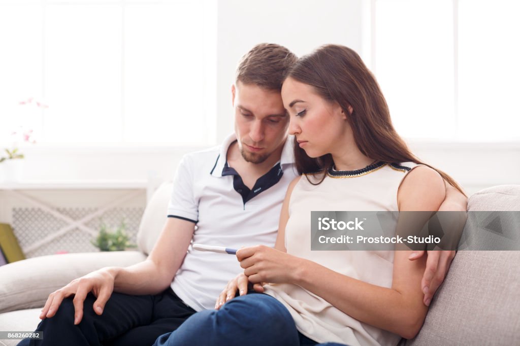 Sad couple after pregnancy test result copy space Sad couple after negative pregnancy test result, sitting on couch at home, copy space Infertility Stock Photo