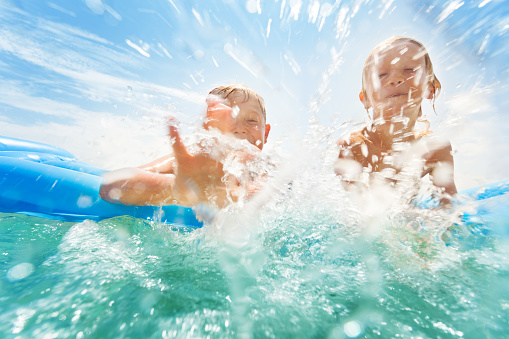 Two boys swim in the sea and splash water in the camera having fun laughing