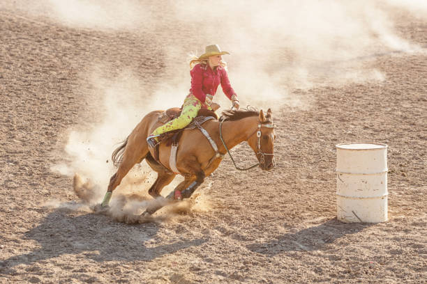 Cowgirl Rodeo Barrel Racing Competition Blonde cowgirl speeding with her horse around white barrel in Barrel Racing Competition inside Rodeo Arena. Rodeo Event, Utah, USA. spanish fork utah stock pictures, royalty-free photos & images
