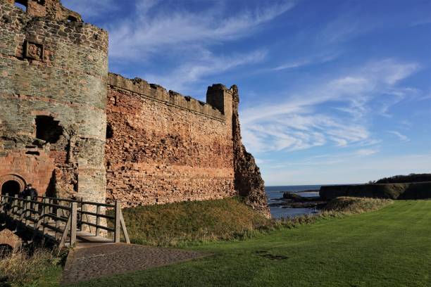 Tantallon Castle North Berwick, East Lothian, Scotland - October 27, 2017: View looking past the entrance and south wing of of Tantallon Castle following the line of the old moat in front of the red sandstone wall. The North Sea is visible in the background in the dip formed by the moat. north berwick scotland east lothian castle scotland stock pictures, royalty-free photos & images