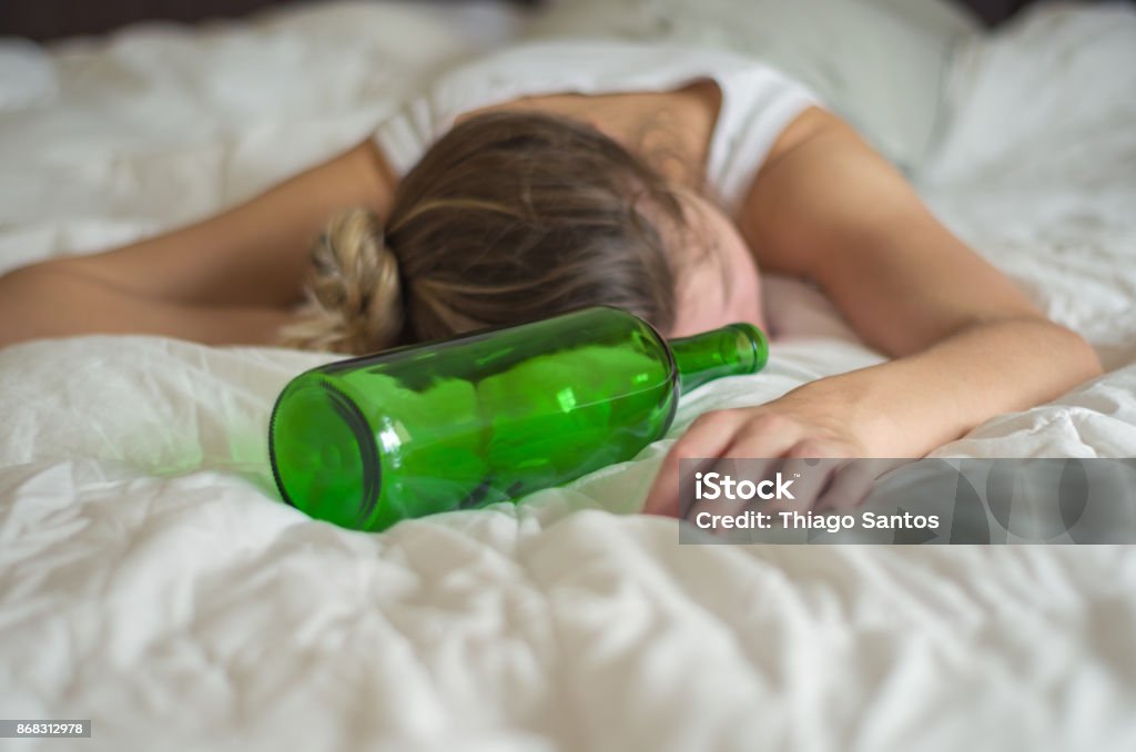 Woman, blond hair, fainted in bed after drinking Great concept of alcohol abuse. Young woman, blond hair, fainted in bed after drinking too much alcohol. Glass of wine in hand, bottle of wine. Women Stock Photo