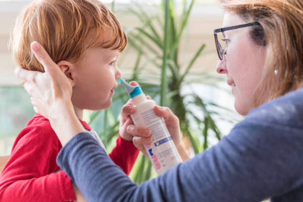 Mom Cleans Baby's Nose With Blower and Saline Nasal Spray Mom Cleans Baby's Nose With Blower and Saline Nasal Spray saline drip stock pictures, royalty-free photos & images