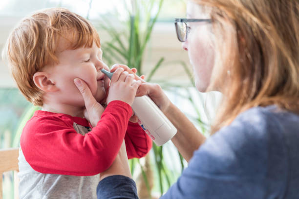 mamá limpia la nariz del bebé con el soplador y el aerosol nasal de solución salino - solución salina fotografías e imágenes de stock