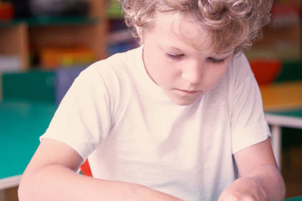 istock Little curly boy is playing something on a table in the kindergarten. 868335580