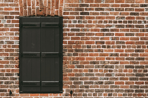 Window covered with wooden black shutters on a brick wall with free space