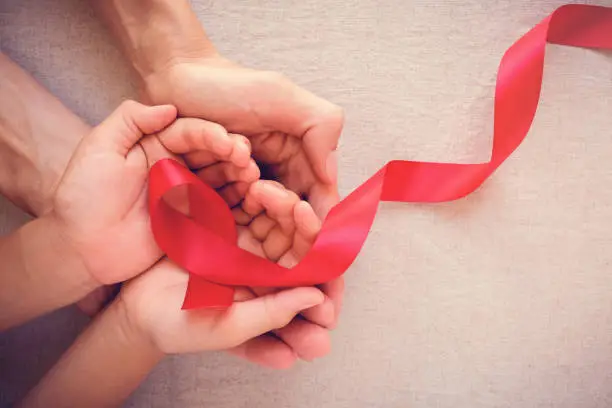 Photo of adult and child hands holding red ribbon, hiv awareness concept, world AIDS day