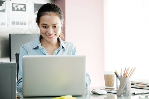 istock Young asian businesswoman working with laptop computer at office table with smiling face, positive emotion, casual office life concept 868365780