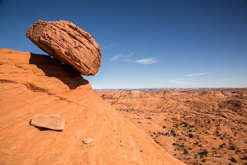 A large sandstone boulder rests precariously over a slope in the desert of the Escalante - Grand Staircase National Monument. The boulder appears to be ready to fall at any moment and slide hundreds of feet into the valley below
