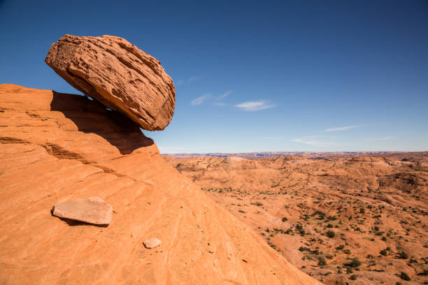 Large balanced boulder looks ready to fall over steep slope A large sandstone boulder rests precariously over a slope in the desert of the Escalante - Grand Staircase National Monument. The boulder appears to be ready to fall at any moment and slide hundreds of feet into the valley below slickrock trail stock pictures, royalty-free photos & images