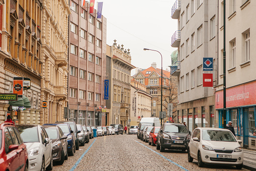 Prague, December 13, 2016: Beautiful street of Prague with old architecture, paving stones, advertising signs and numerous of cars parking along the houses