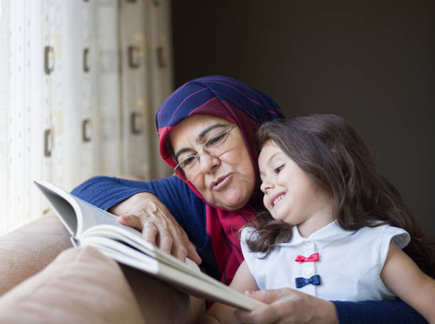 lecture d’un livre avec la petite-fille de grand-mère - grandparent family reading inside of photos et images de collection