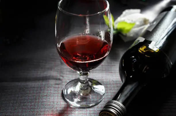 Red wine in a glass and a wine bottle, against a dark background