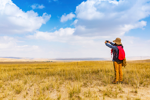 A young woman takes a mobile phone to photograph grassland scenery.