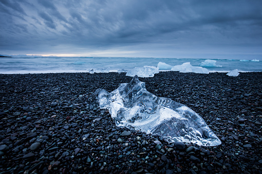 beautiful wiev of iceberg on the black sand by the ocean with dramatic sky. long ekspsiture of moving clouds