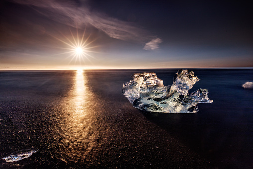 tranquil scene of black sand with iceberg and sun