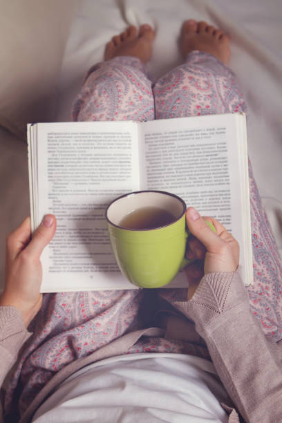 istock Woman sitting on sofa, reading book and drink 868392856