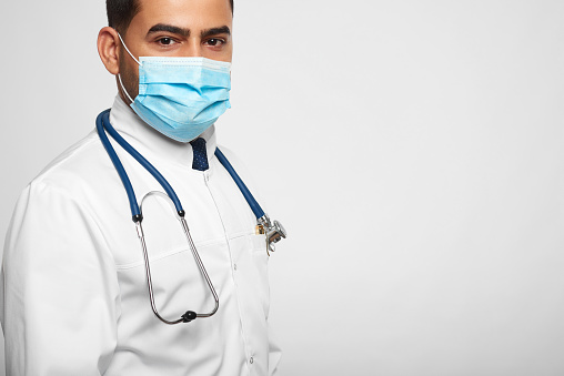 Studio portrait of a male doctor in protective mask posing in a white labcoat looking confidently to the camera copyspace people lifestyle vitality healthcare survey treatment concept.