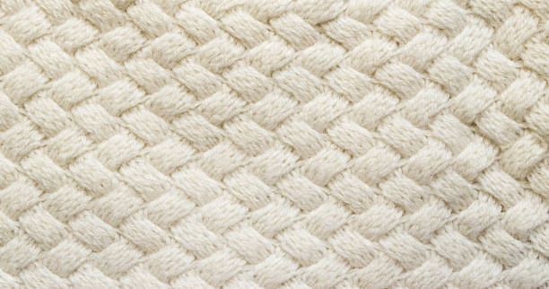 White knitted carpet closeup. Textile texture off white background. Detailed warm yarn background. Knit cashmere beige wool. Natural woolen fabric, sweater fragment.