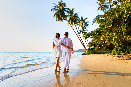 Romantic couple walking together on the tropical beach in warm sunny summer during honeymoon vacations