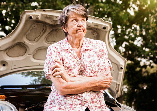 Frustrated old woman with broken-down car grimaces, frustated Senior woman folds her arms and looks up, rolling her eyes in angry frustration about her broken-down car. rolling eyes irritation displeased facial expression stock pictures, royalty-free photos & images