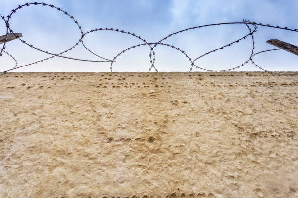 istock Concrete wall with barbed wire on a background of a peaceful blue sky. 868403894