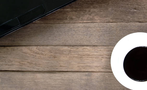 istock White coffee cup and black notebook on rustic wooden table. Black screen smartphone on empty table. 868405382