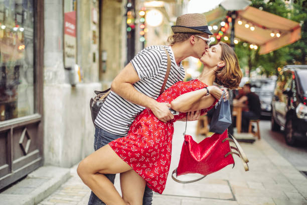 Young couple in love kissing on a bench in summer park. Man wearing shirt with suspenders. Happy future, marriage concepts. Vintage