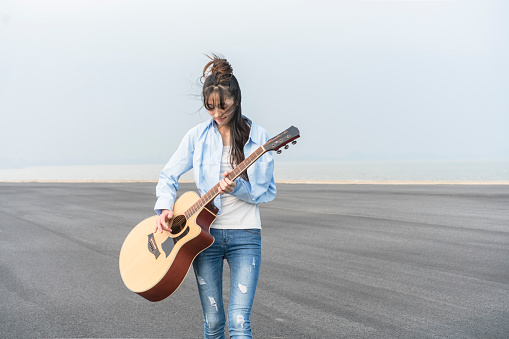 asian woman playing guitar against sky.