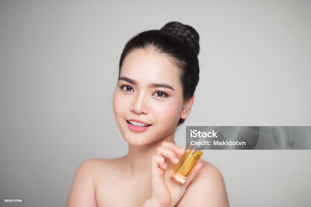 Concept de la beauté. Femme jolie asiatique avec une peau parfaite tenant la bouteille d’huile - Photo de Visage libre de droits
