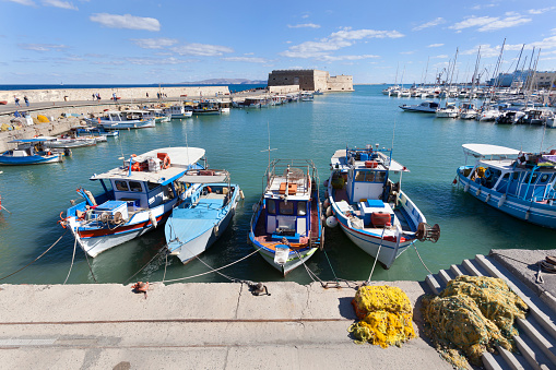 Colorful traditional fishing boats with the fortress in the background in Heraklion harbor on Crete in Greece