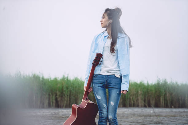 young female carrying guitar walking against sky.