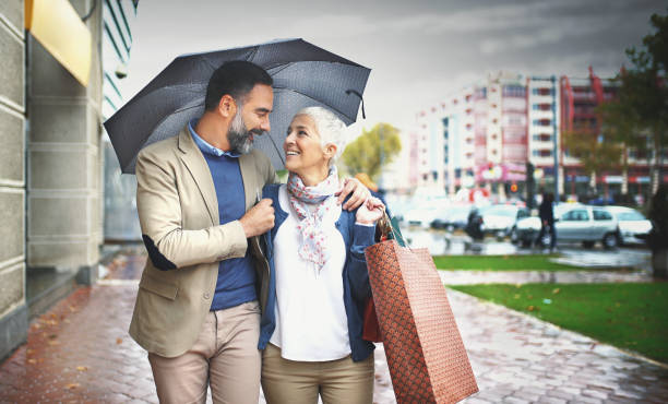 couple âgé milieu marche un jour de pluie. - umbrella senior adult couple autumn photos et images de collection