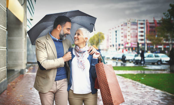 mid aged couple walking on a rainy day. - umbrella senior adult couple autumn imagens e fotografias de stock