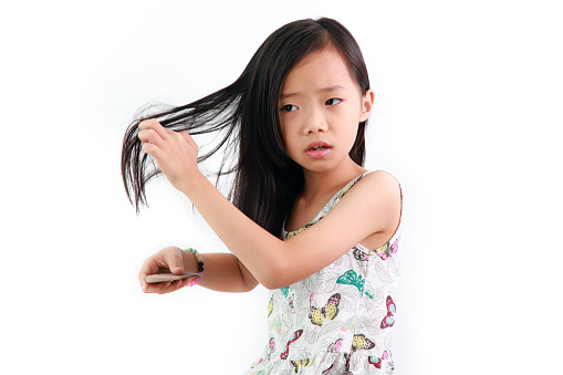 Little Asian girl on a white background with a comb for the hair, the hair problem.