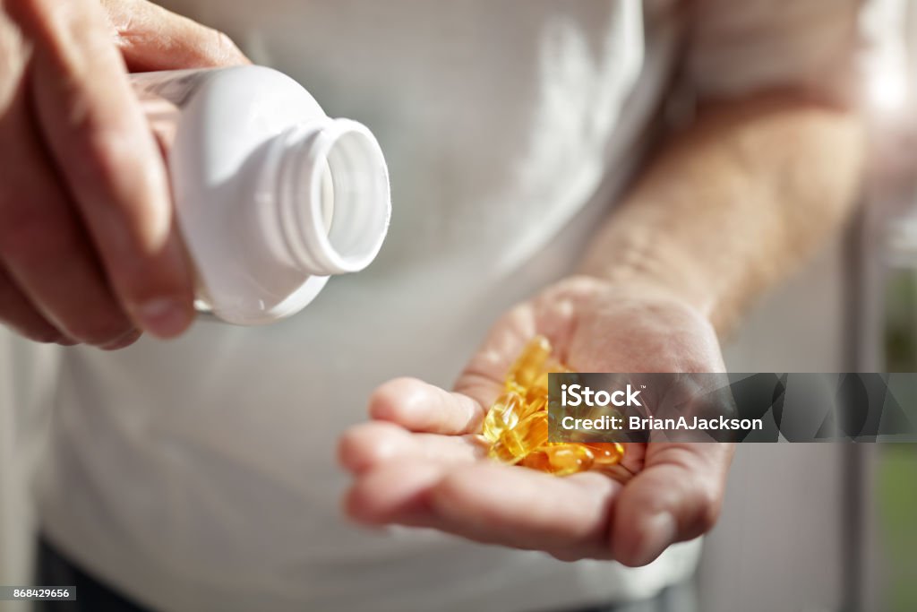 Omega 3 fish oil capsules Bottle of omega 3 fish oil capsules pouring into hand Vitamin D Stock Photo