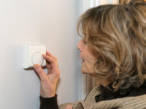 A woman adjusting the central heating thermostat in her home