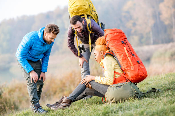 Hikers with backpacks outdoors Young african woman with backpack having a trauma with knee hiking with friends outdoors aids walk stock pictures, royalty-free photos & images