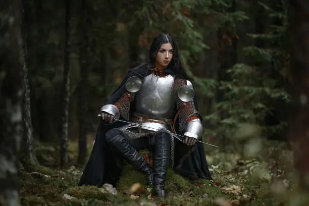 A beautiful warrior girl with a sword wearing chainmail and armor in a mysterious forest