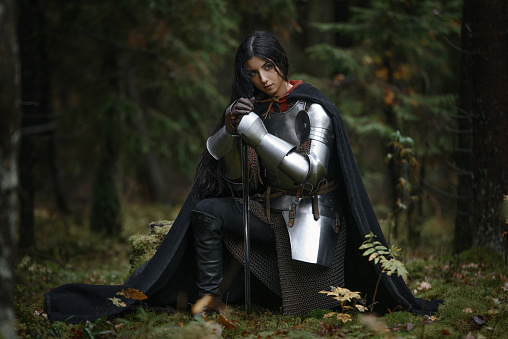 A beautiful warrior girl with a sword wearing chainmail and armor in a mysterious forest