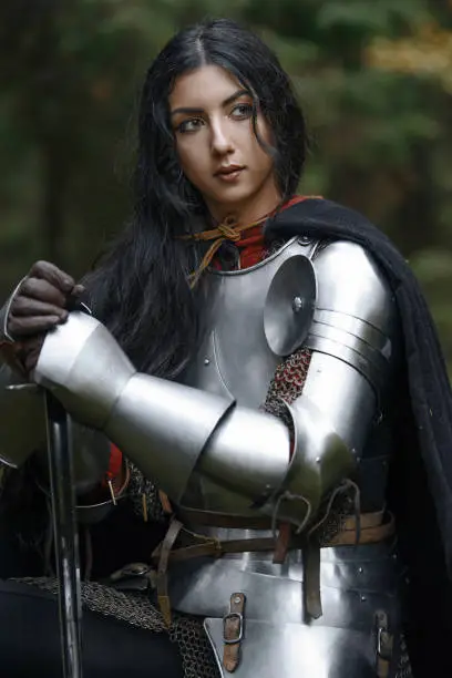 A beautiful warrior girl with a sword wearing chainmail and armor in a mysterious forest