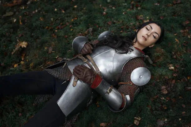 A beautiful warrior girl wearing chainmail and armor lying on the ground in a mysterious forest