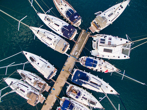 Yachts, sailboats and catamarans moored in port of Poros island in Greece at early morning. Aerial view from drone perspective