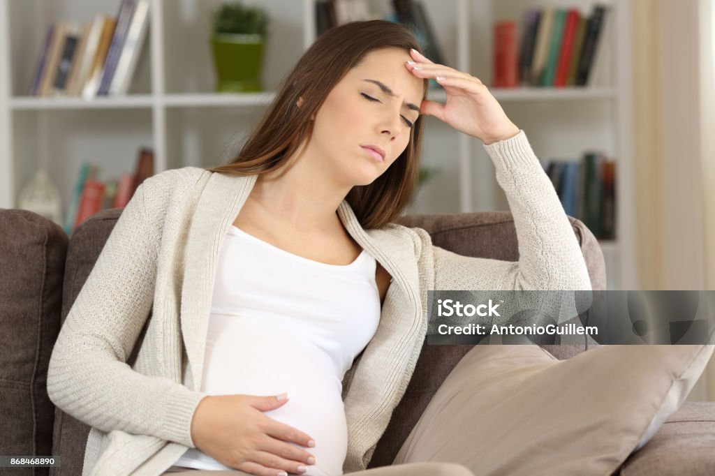Pregnant woman suffering migraine at home Pregnant woman suffering migraine sitting on a sofa at home Pregnant Stock Photo